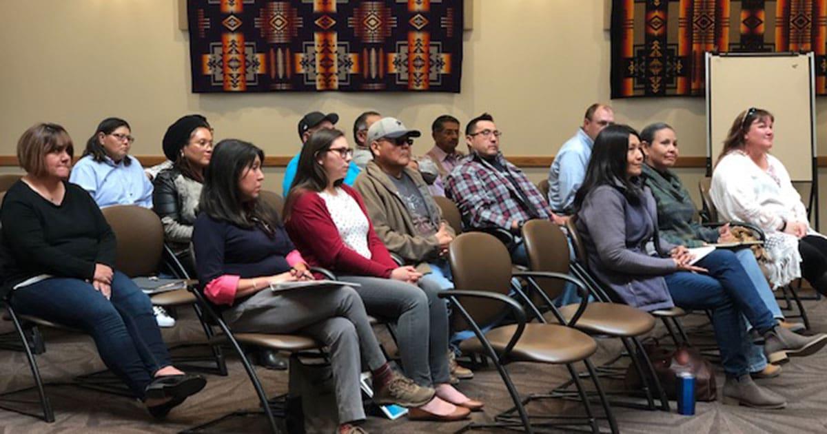 Group of people sit in rows, listening to a speaker.